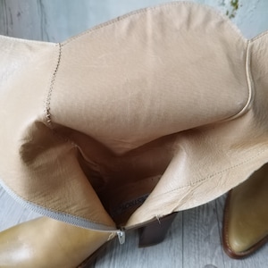 K&ouml;nnte beinhalten: Hellbraune Lederstiefel mit spitzer Zehenpartie und Blockabsatz. Die Stiefel haben einen Rei&szlig;verschluss und ein helles Innenfutter. Das Leder hat einen leichten Glanz, und die Stiefel scheinen ungetragen zu sein. Die Stiefel sind neutral, passend zu verschiedenen Outfits.