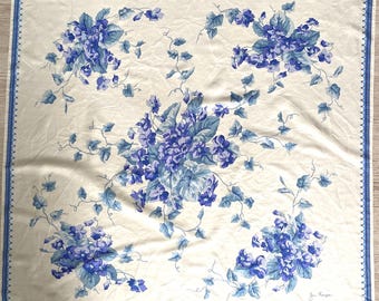Peut inclure: Un foulard carré blanc cassé orné d'un motif répétitif de grappes de fleurs violettes bleues et de feuilles vertes. Le foulard est bordé d'une fine ligne bleue avec un bord festonné. La signature Jim Thompson est imprimée en bas à droite.