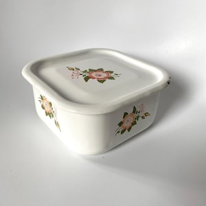 May include: A square white enamel storage container with a matching lid. The exterior and the lid feature a floral pattern consisting of orange and pink flowers with green leaves. The container has rounded corners and a smooth, glossy finish.
