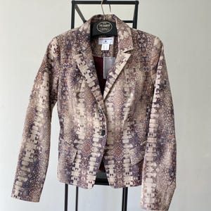 May include: A brown and beige blazer with a snakeskin pattern. The blazer has a single button closure and two pockets. The label on the blazer reads "Rick Cardona".