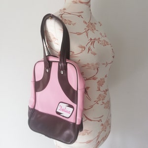 Bolso vintage de vinilo rosa de los años 70 con asa superior, cremallera cuadrada y rayas marrones, tamaño mediano, estilo urbano.