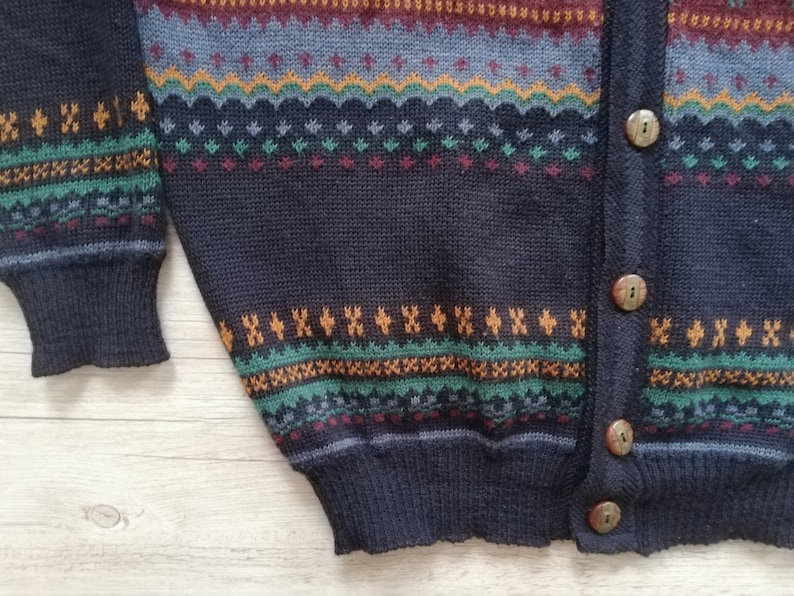 May include: A dark blue knitted cardigan with a colorful geometric pattern. The cardigan has a button closure and long sleeves.