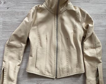 Peut inclure: Une veste en cuir beige dotée d'un col montant, d'une fermeture éclair frontale argentée sur toute la longueur et de manches longues avec des fentes verticales aux poignets. La veste présente des panneaux structurés et des coutures visibles.