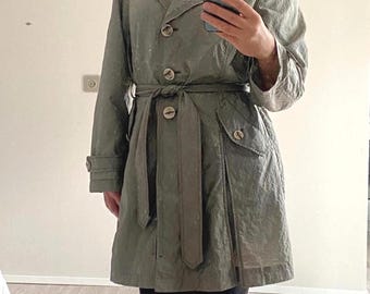 Peut inclure: Un trench-coat vert sauge doté d'un col, de manches longues avec poignets boutonnés et d'une ceinture à nouer assortie. Le manteau présente une fermeture boutonnée sur le devant, deux poches latérales à rabat boutonné et une texture froissée.