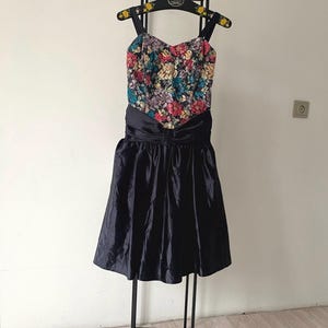 May include: A black velvet dress with a floral embroidered bodice and a black satin sash. The dress has a fitted bodice and a full skirt.