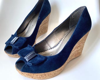 Peut inclure: Une paire de chaussures compensées bleu marine à bout ouvert, dotées d'une texture façon daim, d'une semelle plateforme aspect liège et d'un nœud décoratif sur le devant. La doublure intérieure est argentée avec un bord festonné.