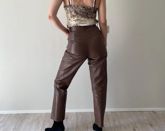 Peut inclure: Un caraco à motif léopard avec de fines bretelles associé à un pantalon taille haute en similicuir marron et des bottines noires. Le pantalon présente une coupe droite et une finition lisse, tandis que le caraco a une texture satinée.