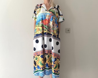 Peut inclure: Une robe mi-longue arborant un imprimé méditerranéen coloré représentant des bâtiments côtiers, des citrons et du feuillage. Le motif comprend une section blanche à gros pois noirs, une bordure orange décorative et un ourlet bleu à motifs.