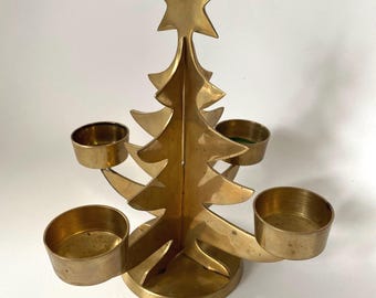 Peut inclure: Un bougeoir en laiton en forme de sapin de Noël stylisé avec une étoile au sommet. La structure présente une silhouette d'arbre verticale centrale montée sur une base circulaire, avec trois bras cylindriques s'étendant pour tenir des bougies.