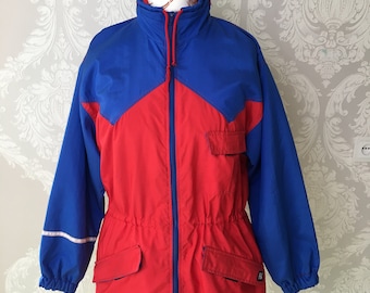 May include: A vintage red and blue jacket with a high collar and a full-length zipper. The jacket has blue sleeves and a red body with two front pockets. A white stripe accents the sleeve. The jacket is displayed on a white mannequin.