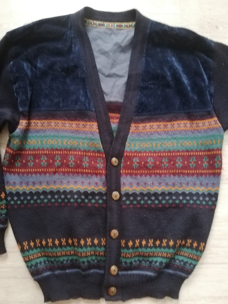 May include: A dark blue cardigan with a colorful striped pattern and brown buttons. The cardigan has a velvet panel on the front.