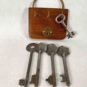 May include: A vintage wooden padlock with a brass handle and keyhole, alongside a silver key and four antique keys. The padlock is made of stained wood and has a brass escutcheon. The keys are made of metal and show signs of age.