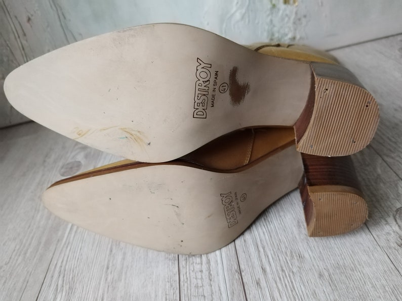 K&ouml;nnte beinhalten: Hellbraune Lederstiefel mit spitzer Zehenpartie und Blockabsatz. Die Sohlen sind hellbeige mit dem Wort "DESTROY" und der Gr&ouml;&szlig;e "41" bedruckt. Hergestellt in Spanien.