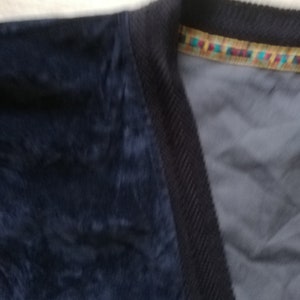 May include: A dark blue corduroy jacket with a colorful trim around the neckline.