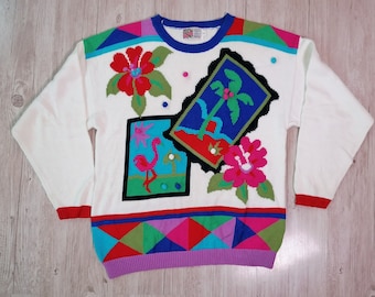 May include: White knitted sweater with a colourful tropical design. The sweater features a flamingo, palm tree, and flowers. The bottom of the sweater has a geometric pattern in red, green, blue, and pink.