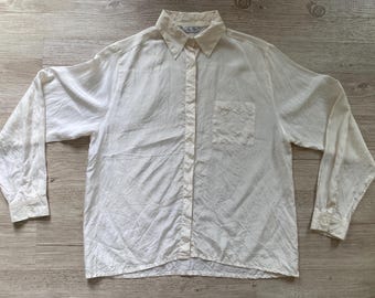 Peut inclure: Une chemise à manches longues boutonnée de couleur blanc cassé. La chemise présente un col classique, une poche poitrine unique sur le côté gauche et des poignets boutonnés. Le tissu a une texture subtile et un aspect légèrement froissé.