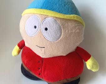 Peut inclure: Une peluche représentant le personnage Eric Cartman de South Park. La figurine porte un bonnet bleu avec un bord et un pompon jaunes, une veste rouge avec des boutons noirs, un pantalon marron et des chaussures noires. Visage rond et grands yeux blancs.