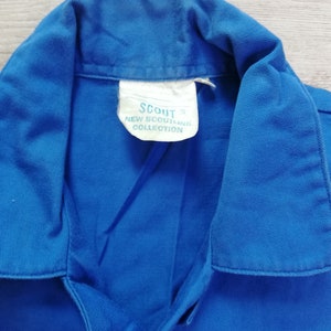 Pode incluir: Uma camisa azul de colarinho com uma etiqueta branca que diz "Scout New Scoutline Collection".