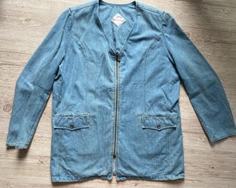 Peut inclure: Une veste en jean bleu clair avec une encolure en V et une fermeture éclair frontale intégrale. La veste présente des manches longues, deux poches avant à rabat boutonné et une étiquette blanche au col avec le texte "Sybille Welschland".