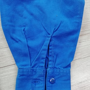 Pode incluir: Close-up de uma camisa azul de manga comprida com punho de bot&atilde;o. O punho tem um &uacute;nico bot&atilde;o e uma pequena fenda na lateral.
