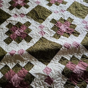 May include: A quilted blanket with a checkered pattern in shades of green, white, and pink. The quilt is made with a variety of fabrics and textures, creating a unique and interesting design.