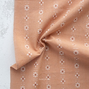 May include: A close-up of a peach-colored fabric with a white floral pattern. The fabric has a subtle texture and a slightly wrinkled appearance.