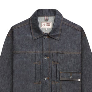 Op de afbeelding: Een donkerblauw denim jack met knoopsluiting, twee voorzakken en een borstzak. Het jack heeft een label met de tekst "Free Denim" met een gestileerd "F"-logo.