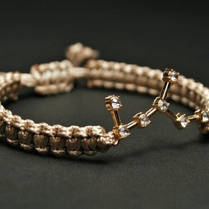 Peut inclure: Un bracelet tress&eacute; beige avec un charme de constellation dor&eacute;e orn&eacute; de strass transparents.