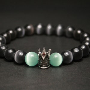 May include: Black and gray beaded bracelet with a silver crown charm and two light green beads.