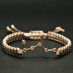 Peut inclure: Un bracelet tress&eacute; beige avec un charme de constellation dor&eacute;e orn&eacute; de strass transparents.