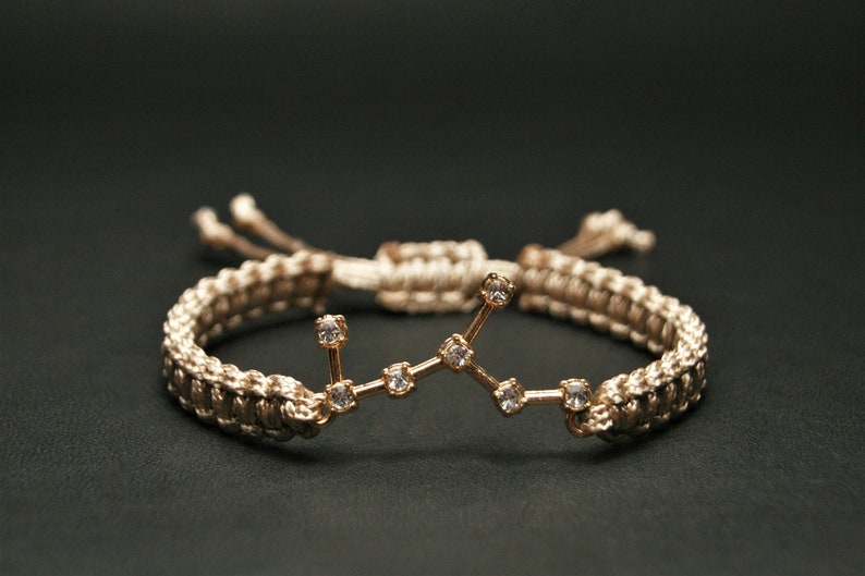 Peut inclure: Un bracelet tress&eacute; beige avec un charme de constellation dor&eacute;e orn&eacute; de strass transparents.