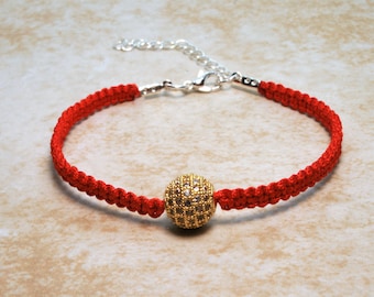 May include: Red string bracelet with a gold-toned, round bead encrusted with small, clear rhinestones. The bracelet has a silver clasp.