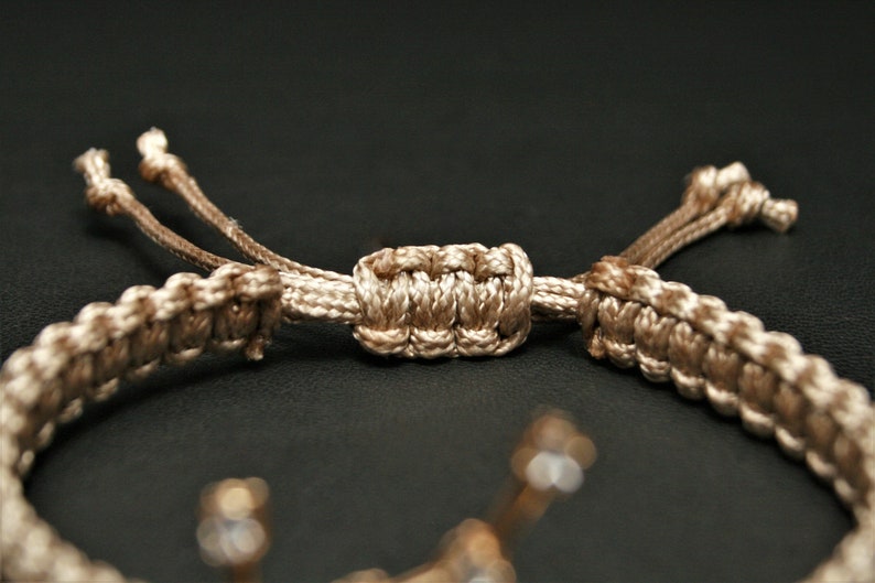 Peut inclure: Un bracelet tress&eacute; beige avec une fermeture nou&eacute;e. Le bracelet est fait d'un cordon &eacute;pais et tiss&eacute; et a un design simple et &eacute;l&eacute;gant.