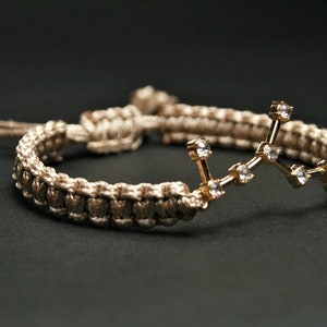 Peut inclure: Un bracelet tress&eacute; marron et beige avec un charme de constellation dor&eacute;e orn&eacute; de strass transparents.