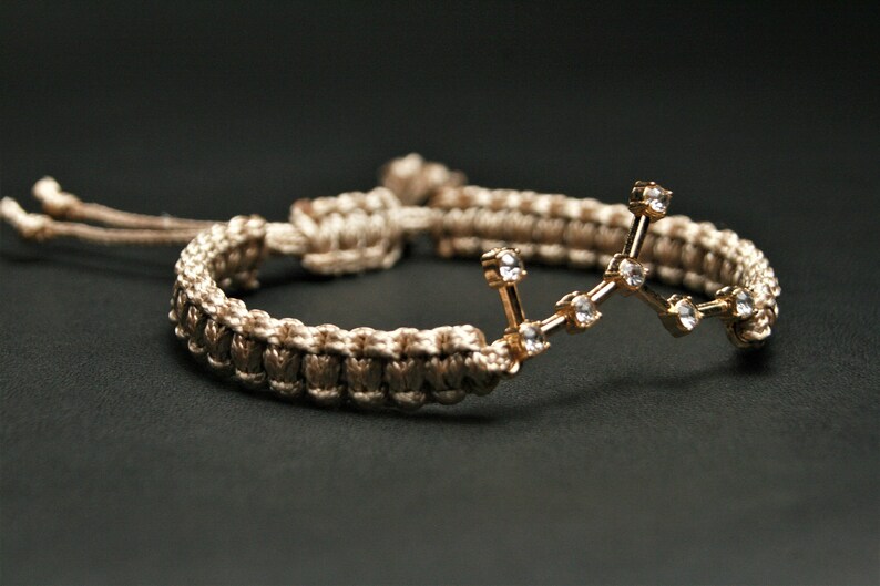 Peut inclure: Un bracelet tress&eacute; marron et beige avec un charme de constellation dor&eacute;e orn&eacute; de strass transparents.