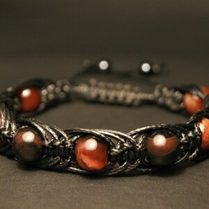 Puede incluir: Un brazalete trenzado negro con cuentas de ojo de tigre rojo y marrón.