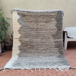 May include: A rectangular, hand-woven rug with a gradient design. The rug transitions from white to gray and brown, with horizontal stripes. Tassels adorn the bottom edge. This rug is suitable for home decor.