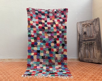 May include: A colourful Moroccan rug with a chequered pattern in shades of red, blue, green, and pink. The rug is made of wool and has a fringed edge.