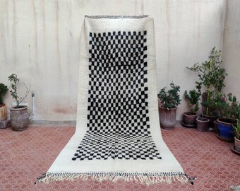 May include: A black and white checkered rug with a fringe border. The rug is made of wool and has a traditional Moroccan design.