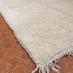 May include: A white shag rug with a fringe border. The rug is made of wool and has a soft, fluffy texture.