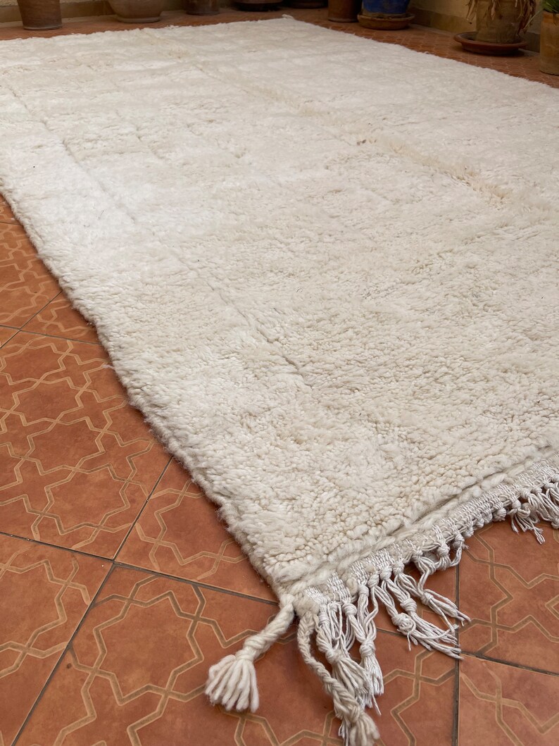 May include: A white shag rug with a fringe border. The rug is made of wool and has a soft, fluffy texture.