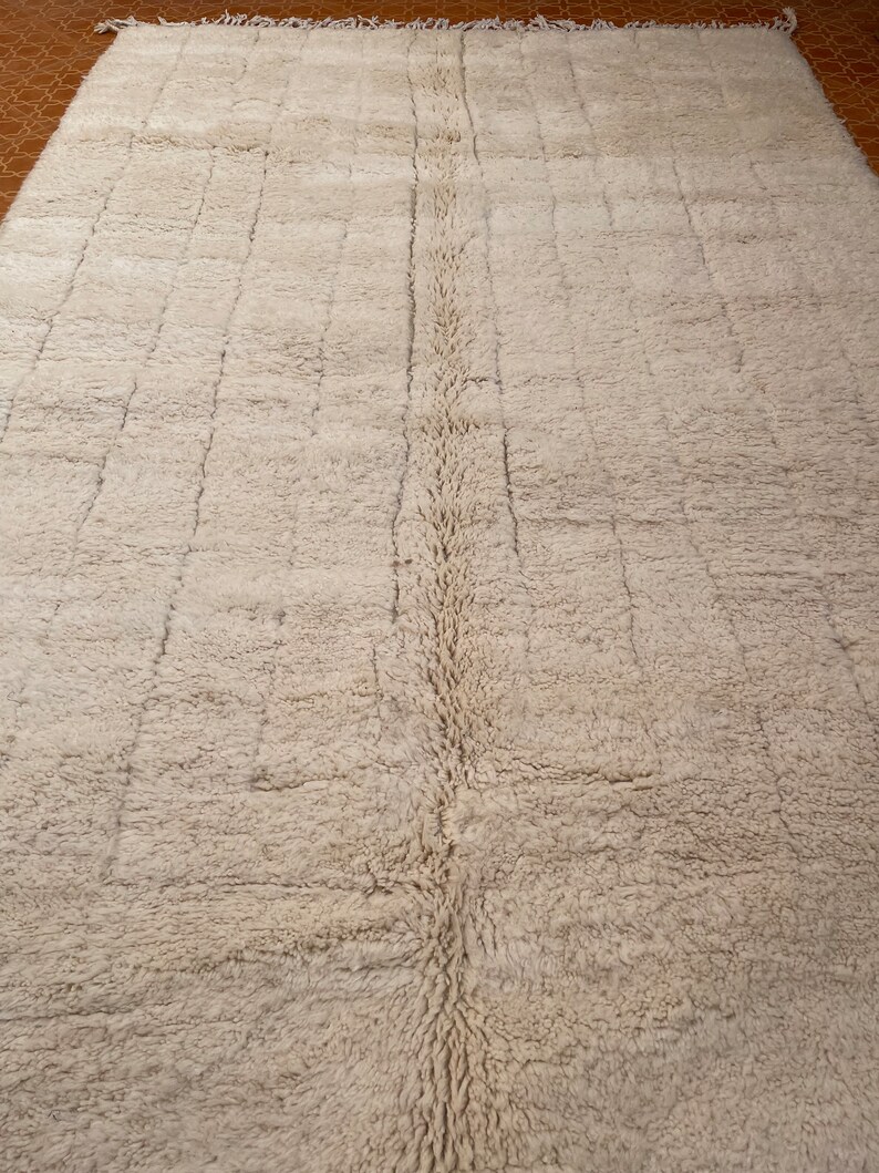 May include: A white, fluffy rug with a subtle woven pattern. The rug has a long, narrow shape and a fringe border.