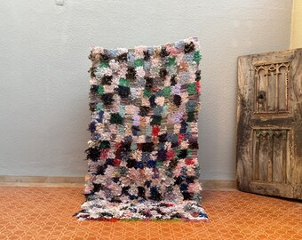 May include: A colourful Moroccan rug with a patchwork design. The rug is made of wool and has a fringe border. It is hanging on a wall in a room with a wooden door.
