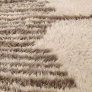 May include: Close-up of a textured rug with a cream-colored background and brown, horizontal stripe patterns. The rug has a soft, plush appearance, suggesting a comfortable and decorative home textile.