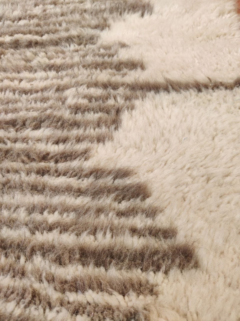 May include: Close-up of a textured rug with a cream-colored background and brown, horizontal stripe patterns. The rug has a soft, plush appearance, suggesting a comfortable and decorative home textile.