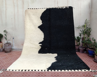 May include: A large, rectangular rug with a striking two-tone design. One half is a creamy white, the other a deep black. The rug's texture appears plush and woven, with a fringe detail along the bottom edge. The rug is displayed indoors.