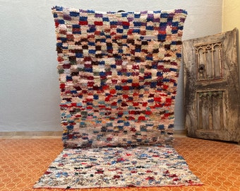 May include: A colourful Moroccan rug with a chequered pattern in shades of red, blue, white, and brown. The rug is made of wool and has a hand-woven texture.