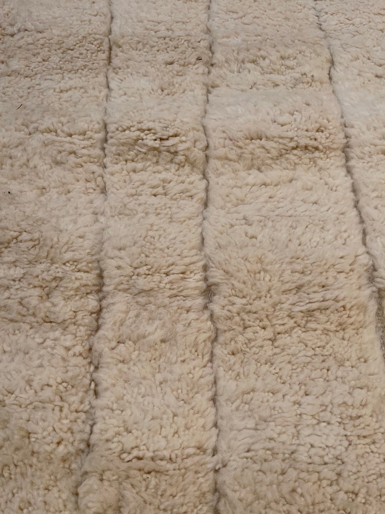 May include: A close-up of a white, fluffy rug with a textured, woven pattern. The rug has a soft, plush feel and is made of natural fibres.