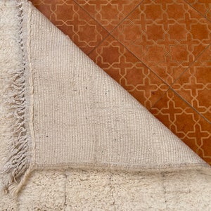 May include: A white, fluffy rug with a fringe border. The rug is folded over, revealing the woven backing.