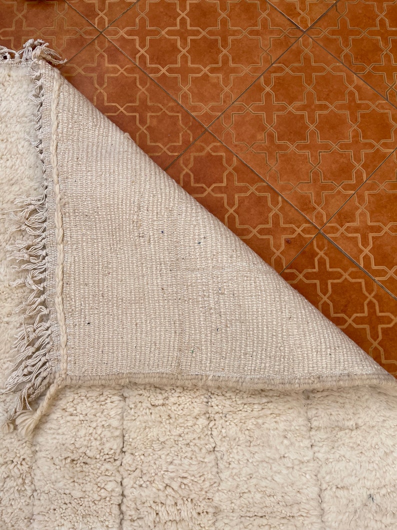 May include: A white, fluffy rug with a fringe border. The rug is folded over, revealing the woven backing.